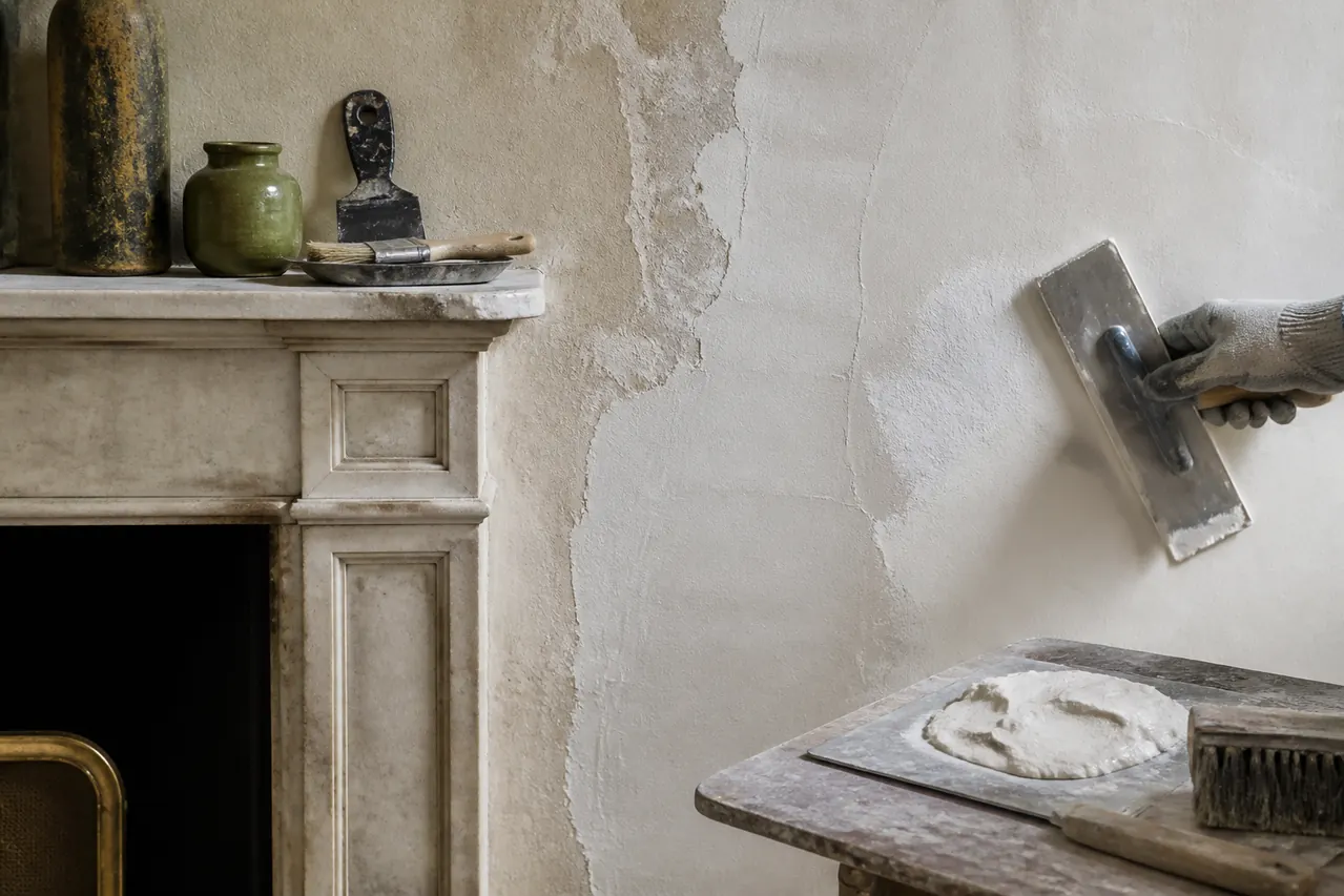 Application d’enduit sur un mur intérieur près d’une cheminée ancienne